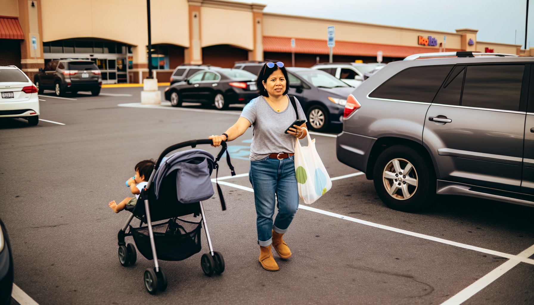 A mom walking through a grocery store parking lot with her phone and stroller — relaxed and in control of her day.